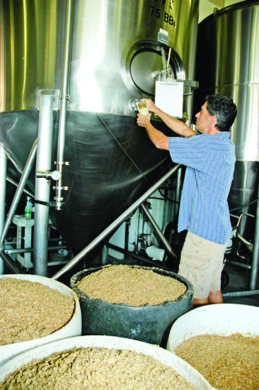 Brewmaster Rich Tucciarone pulls a sample of fermenting beer for quality assurance while bins of spent grain await shipment to Palani Ranch for cattle feed.