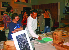 (HO’IKE: display or show)—HOEA student from California, Geoffrey Mundon, center, shows the collection of his works made during the studio program to HOEA Steering Committee member, Fran Sanford, at left. Another HOEA student, Tara Gumapac, right, also studies the work.