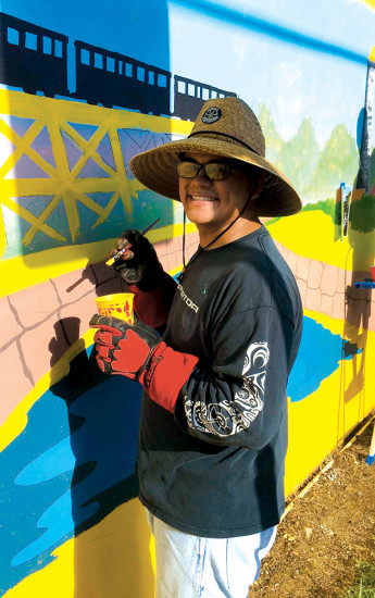 Elijah painting the train on the Hāwi Post Office mural with Patrick Ching. photo courtesy of Sarina Seidel