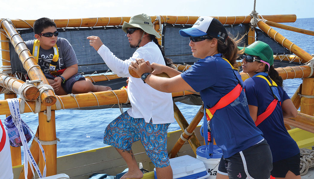 Crew member and teacher Rod Floro explains navigation to Tyler Uehara, while crew member Kailin Kim shows teacher Kanana Kuhaulua how to steer the canoe.