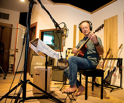 Barefoot in his high-tech studio, Charles plays the guitar track for a new song.
