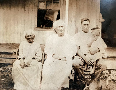 (R-L) Luka Hale on her father's lap, Isaac Kepo‘okalani Hale, Sr.; Mele Hale, Isaac Sr.'s mother; and Kaho‘omaeha Kapukini, Mele's mother. photo from the Lyman Museum Archives