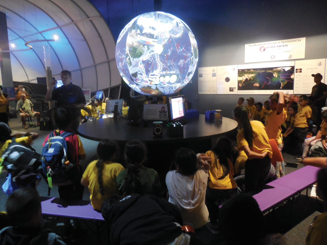 Educational Programs Coordinator Punawai Rice leads a Science On A Sphere (SOS) presentation for ‘Ele‘ele Elementary School fourth graders from Kaua‘i Island inside ‘Imiloa Astronomy Center’s exhibit hall. Using computer-generated images and video projectors, the six-foot-diameter spherical screen is populated with visual data including earthquakes, passenger aircraft routes, sea surface currents and temperatures, climate change time-lapses, and sea ice concentrations. photo by Stefan Verbano