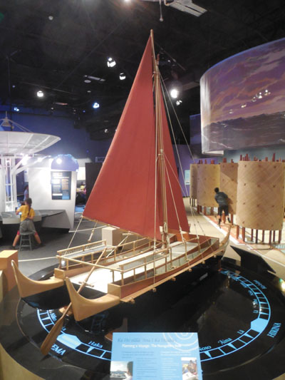 A model double-hulled voyaging canoe, on display atop a star compass showing the Hawaiian names of cardinal directions. photo by Stefan Verbano