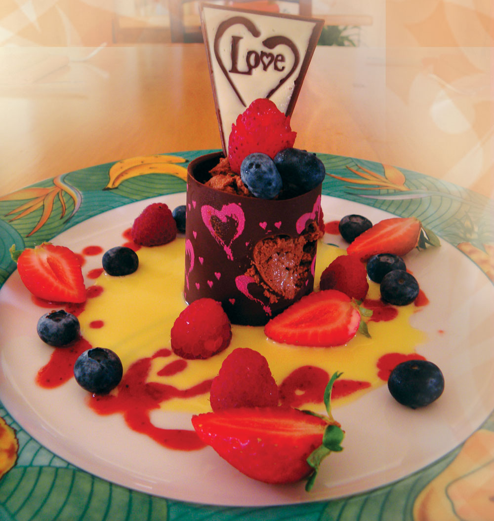 Chocolate shell with heart cut-out, filled with Chocolate mousse on a pool of vanilla sauce with strawberry coulis, garnished with Waimea strawberries and blueberries: for special occasions such as anniversaries!