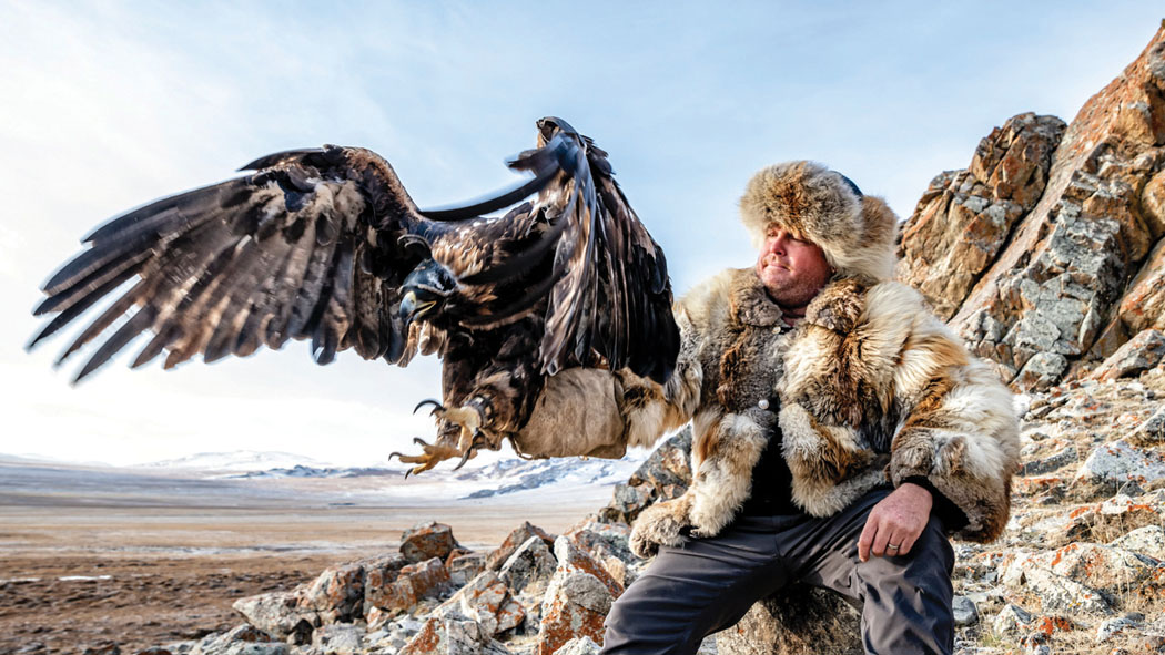 CJ steps into the photo from time to time, shown here in Mongolia in falconer’s gauntlet holding a huge eagle. photo courtesy of CJ Kale