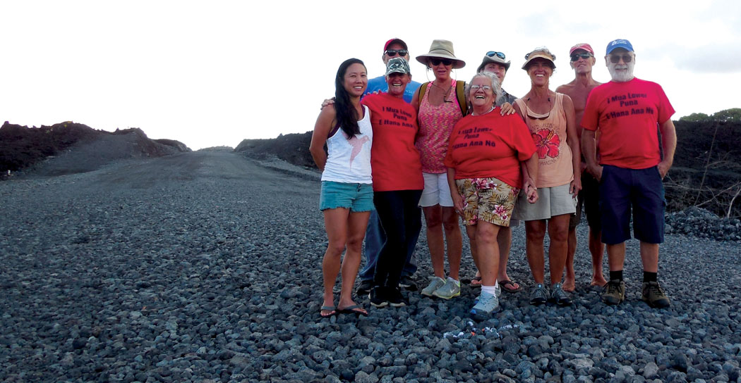 A group of smiling Lower Puna residents stand along the road of freshly laid crushed gravel leading south to the pre-eruption site of “Four Corners” (intersection of Highways 132 and 137) on the Kapoho coastline. Most either lost or were cut off from their homes due to lava flows from the 2018 Lower Puna Eruption, and many have eagerly awaited the County’s reopening of Highway 132 and safe, convenient access to their land after more than one and a half years of isolation. Note: center-right of the photo shows the still-green upper slopes of Green Lake Mountain, which was spared from lava inundation. photo by Stefan Verbano