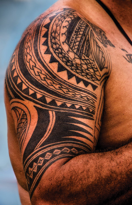 Tattoo featuring a combination of Polynesian elements, including shark teeth, spearheads, ocean waves, and a line of enata (human figures) representing family and a.ncestors guarding their descendants